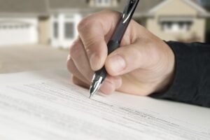 real estate lawyer Anaheim, CA with a closeup of a hand signing a contract and a home in the background